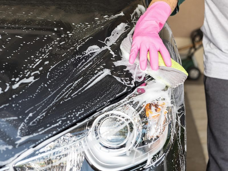 A hand washing a car with a soapy sponge